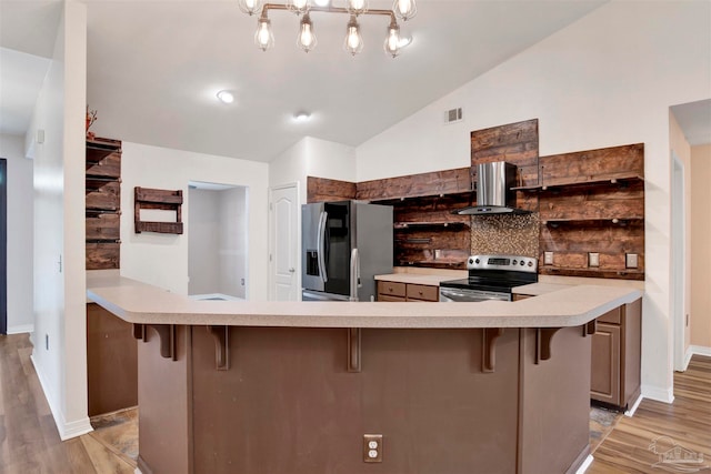 kitchen featuring stainless steel appliances, light wood-type flooring, wall chimney exhaust hood, a kitchen bar, and vaulted ceiling