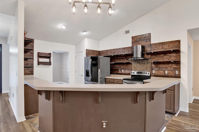 kitchen with wall chimney range hood, stainless steel appliances, backsplash, and a breakfast bar area