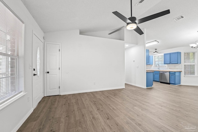 unfurnished living room featuring ceiling fan with notable chandelier, lofted ceiling, sink, light wood-type flooring, and a textured ceiling