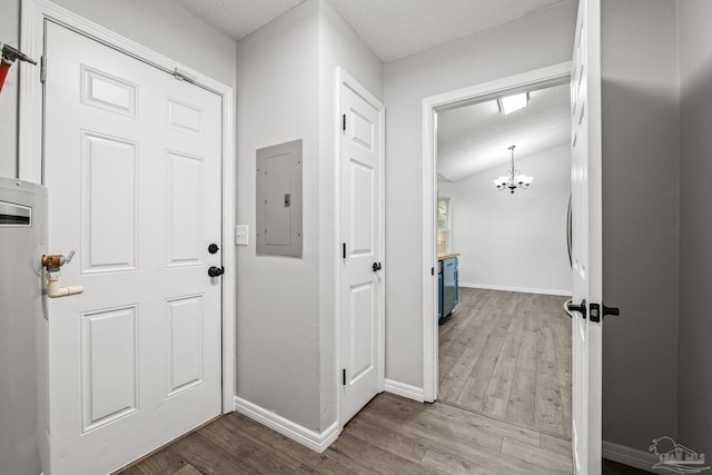 corridor featuring wood-type flooring, lofted ceiling, a chandelier, electric panel, and a textured ceiling