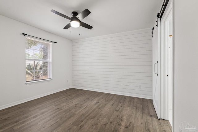 interior space featuring hardwood / wood-style flooring, a barn door, ceiling fan, and wood walls