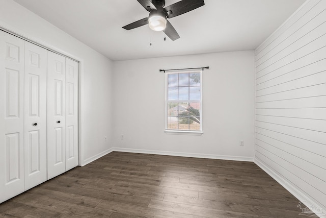 unfurnished bedroom featuring ceiling fan, dark hardwood / wood-style flooring, a closet, and wood walls