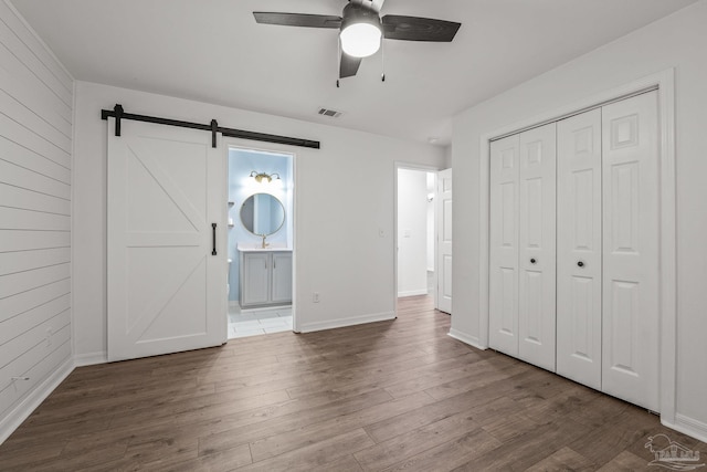 unfurnished bedroom featuring a closet, dark wood-type flooring, a barn door, and wood walls