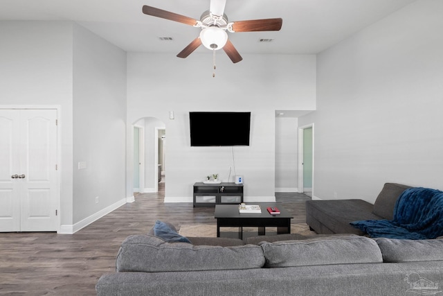 living area featuring visible vents, baseboards, a towering ceiling, wood finished floors, and arched walkways