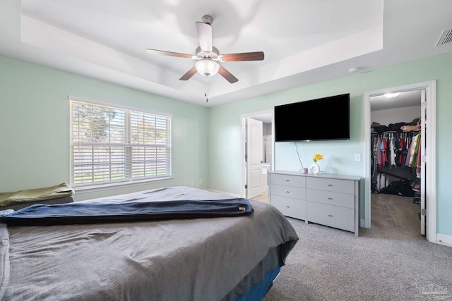 bedroom with visible vents, a tray ceiling, a closet, light carpet, and a walk in closet