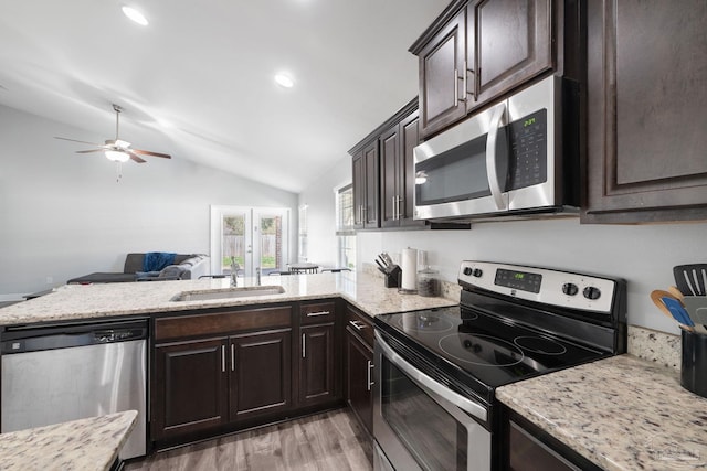 kitchen featuring dark brown cabinets, vaulted ceiling, a peninsula, stainless steel appliances, and a sink