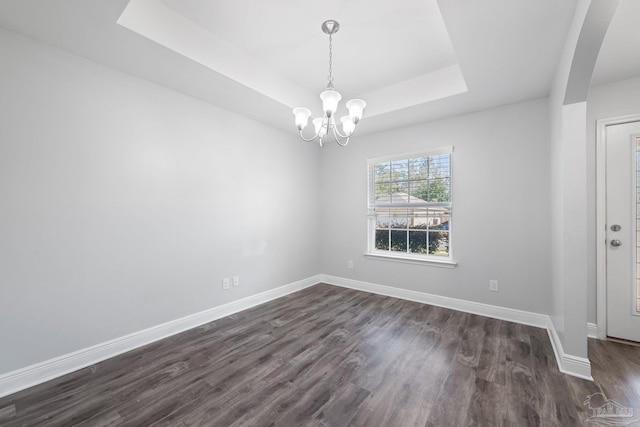 spare room with a chandelier, a raised ceiling, baseboards, and dark wood-style flooring