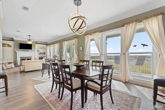 dining room featuring ceiling fan, a fireplace, visible vents, ornamental molding, and light wood finished floors