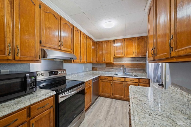 kitchen featuring light stone countertops, under cabinet range hood, appliances with stainless steel finishes, brown cabinetry, and a sink