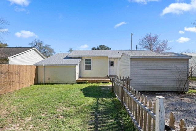 back of property with a lawn, a wooden deck, an outdoor structure, and fence