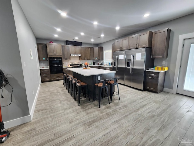 kitchen with a center island, light hardwood / wood-style flooring, dark brown cabinets, a kitchen bar, and stainless steel appliances