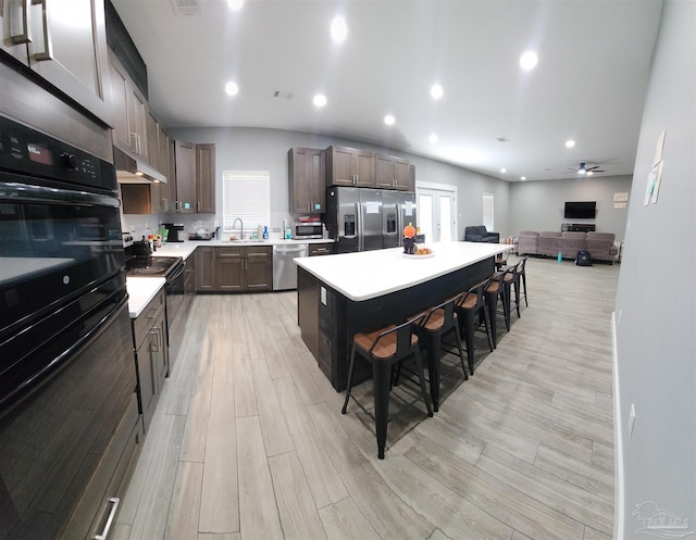 kitchen featuring ceiling fan, a center island, stainless steel appliances, light hardwood / wood-style flooring, and a kitchen bar