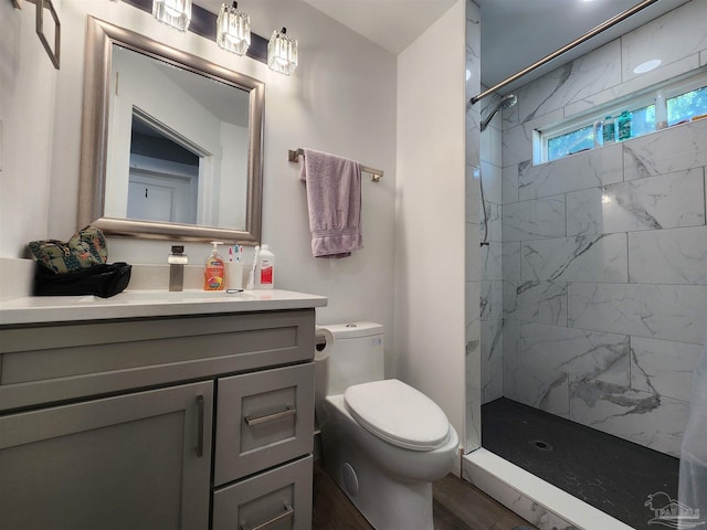 bathroom with a tile shower, hardwood / wood-style floors, vanity, and toilet