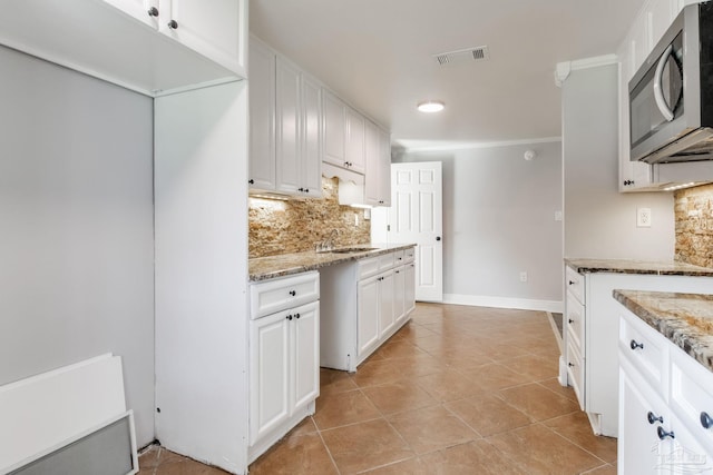 kitchen featuring sink, light tile patterned floors, white cabinetry, backsplash, and light stone counters