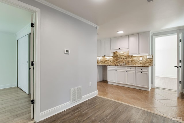 kitchen with white cabinetry, decorative backsplash, crown molding, light stone countertops, and light wood-type flooring