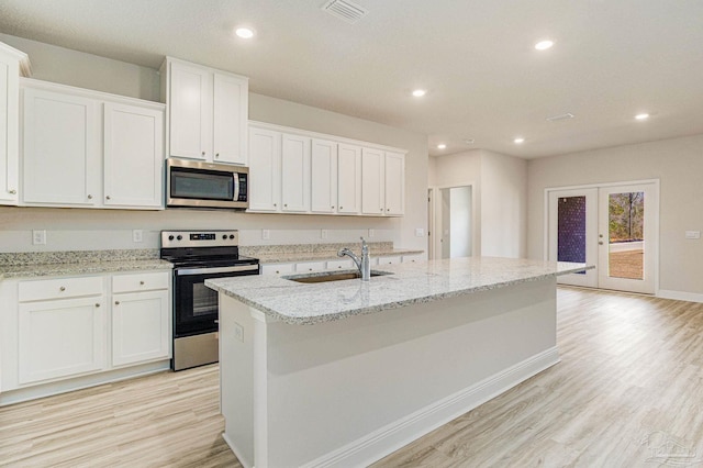 kitchen featuring light wood finished floors, stainless steel appliances, visible vents, a kitchen island with sink, and a sink