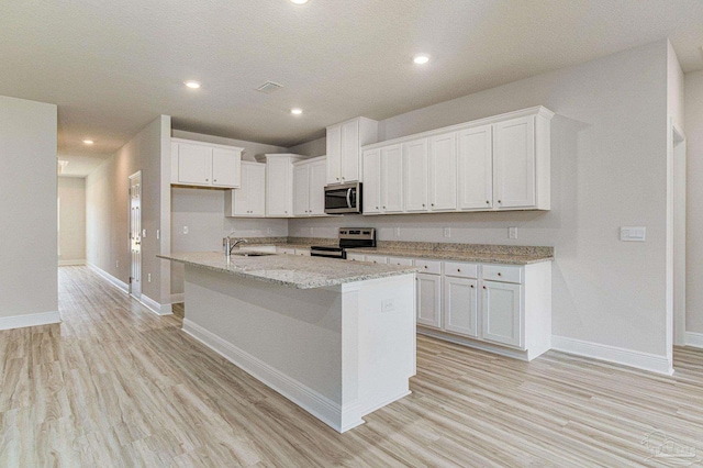 kitchen featuring a center island with sink, baseboards, white cabinets, appliances with stainless steel finishes, and light wood-style floors