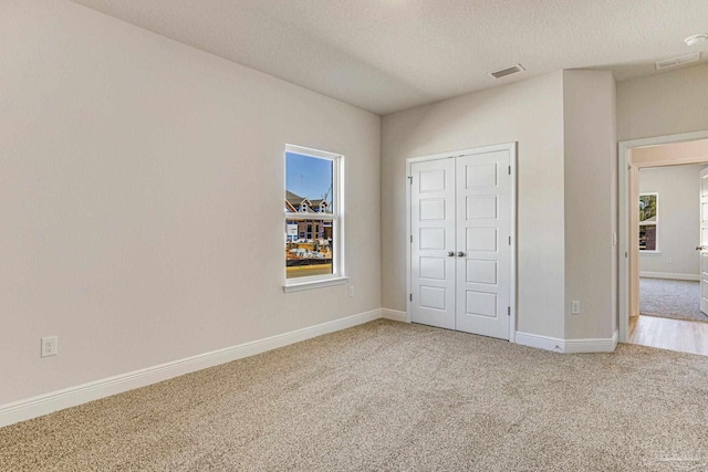 unfurnished bedroom with baseboards, visible vents, a textured ceiling, carpet flooring, and a closet