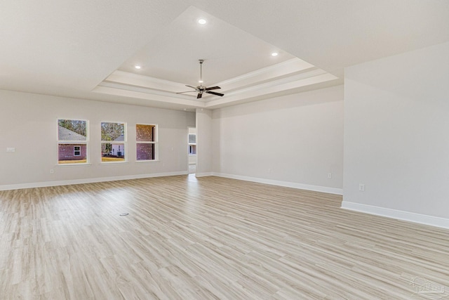 unfurnished living room with a tray ceiling, recessed lighting, a ceiling fan, light wood-style floors, and baseboards