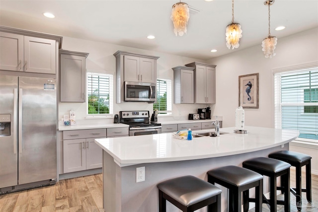 kitchen with light wood-type flooring, a kitchen island with sink, stainless steel appliances, sink, and a breakfast bar area