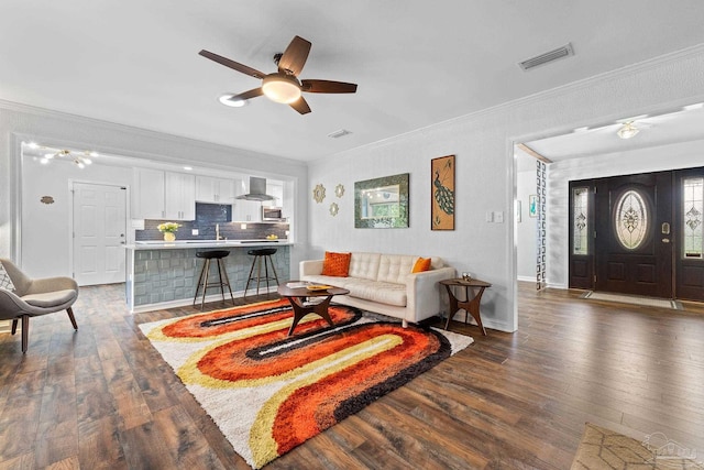 living room with ceiling fan, dark wood finished floors, visible vents, and crown molding