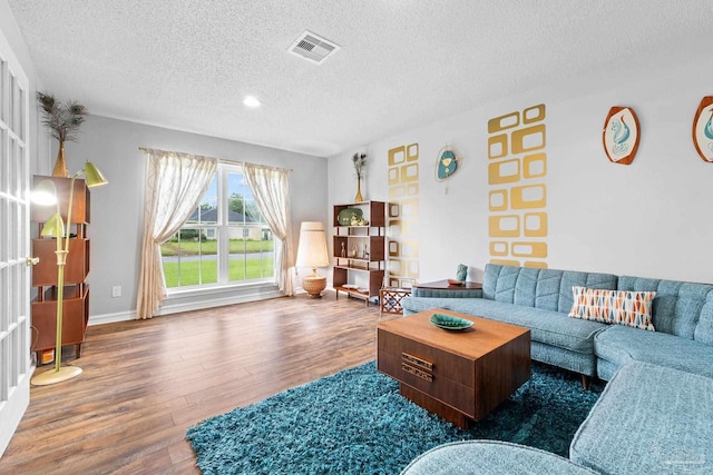 living area featuring visible vents, a textured ceiling, baseboards, and wood finished floors