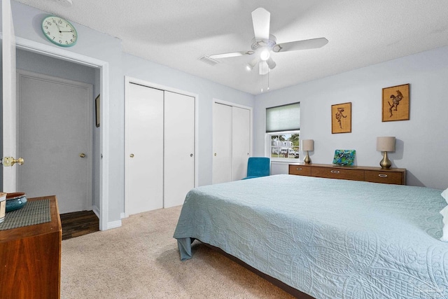 bedroom featuring ceiling fan, a textured ceiling, carpet flooring, visible vents, and multiple closets