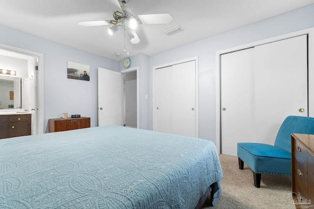 bedroom featuring light colored carpet, a ceiling fan, two closets, visible vents, and ensuite bath