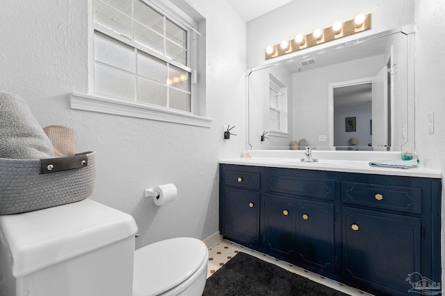 bathroom featuring visible vents, a textured wall, toilet, vanity, and baseboards