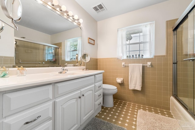 full bathroom featuring tile walls, bath / shower combo with glass door, visible vents, toilet, and vanity