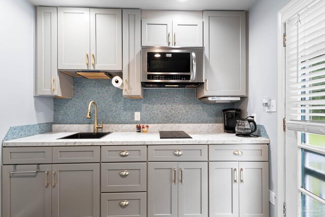 kitchen featuring decorative backsplash, stainless steel microwave, a sink, and gray cabinetry