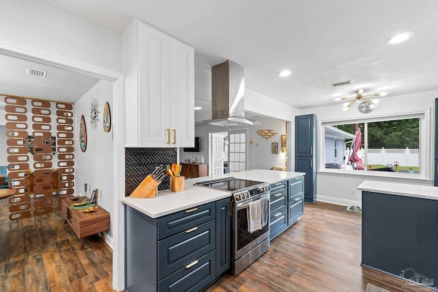 kitchen featuring visible vents, wall chimney exhaust hood, stainless steel electric range oven, blue cabinets, and light countertops