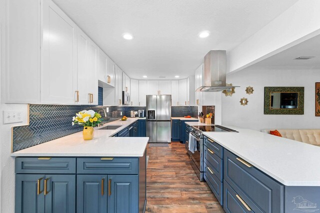 kitchen featuring a peninsula, island range hood, appliances with stainless steel finishes, and light countertops