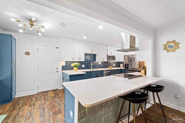 kitchen featuring blue cabinets, white cabinetry, light countertops, appliances with stainless steel finishes, and wall chimney exhaust hood