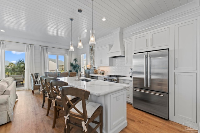 kitchen with backsplash, light wood-type flooring, custom range hood, a kitchen bar, and stainless steel built in fridge