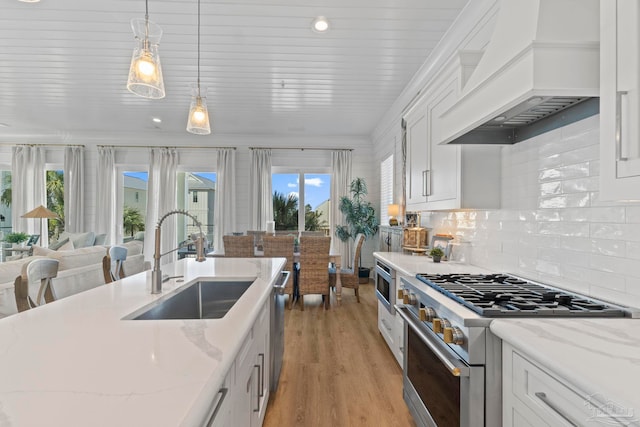 kitchen with premium range hood, a sink, stainless steel appliances, white cabinets, and light wood-type flooring