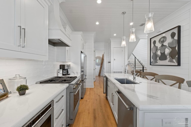 kitchen featuring premium range hood, high quality appliances, a kitchen island with sink, a sink, and white cabinets