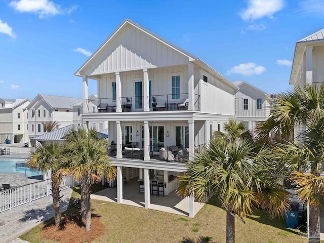 rear view of house with board and batten siding, fence, a balcony, a patio area, and an outdoor pool