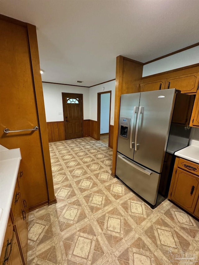 7920 Reeders Ln, Pensacola, FL 32526 - kitchen with stainless steel fridge with ice dispenser, brown cabinetry, wainscoting, light countertops, and wood walls