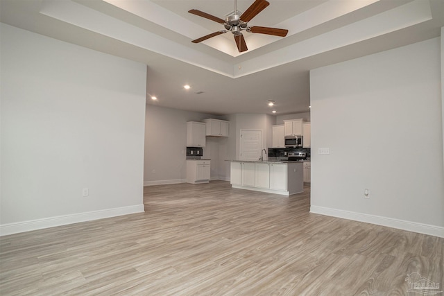 unfurnished living room with ceiling fan, a raised ceiling, light wood-style floors, recessed lighting, and baseboards