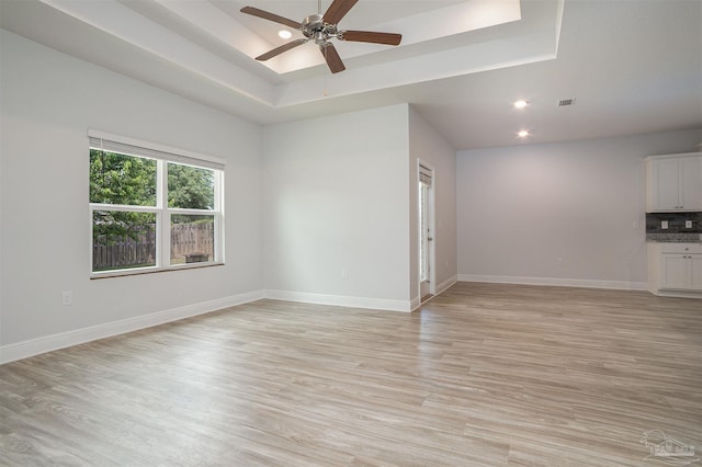 unfurnished living room with light wood finished floors, a ceiling fan, baseboards, a tray ceiling, and visible vents