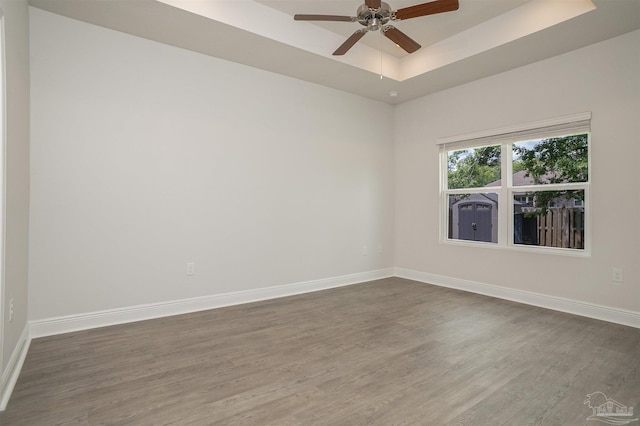 spare room featuring baseboards, a tray ceiling, dark wood-style floors, and ceiling fan