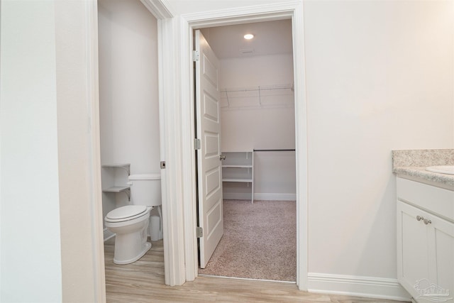 bathroom with wood finished floors, vanity, baseboards, toilet, and a spacious closet
