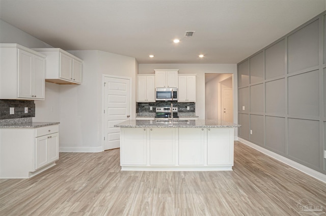 kitchen with a kitchen island with sink, stainless steel appliances, decorative backsplash, and light wood-style flooring