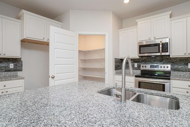 kitchen featuring light stone countertops, white cabinets, a sink, appliances with stainless steel finishes, and backsplash