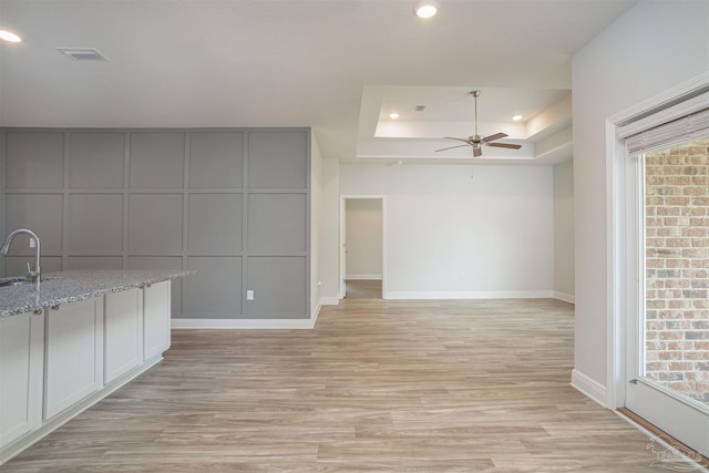 interior space with visible vents, light wood-style floors, ceiling fan, a raised ceiling, and a sink