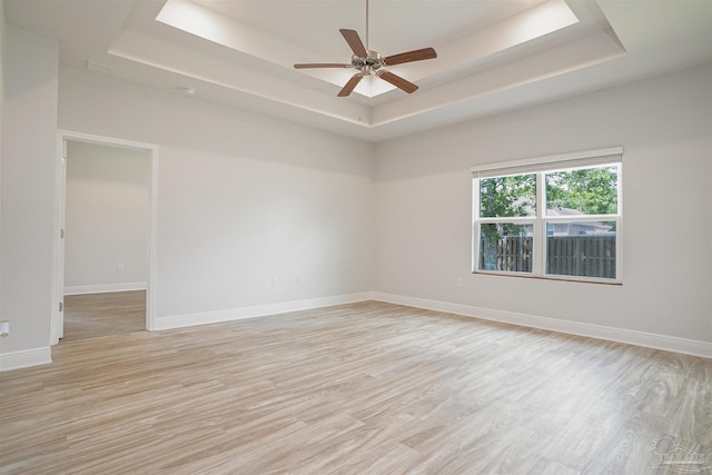 spare room with baseboards, ceiling fan, a tray ceiling, and light wood-type flooring