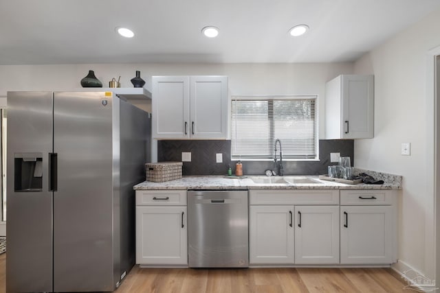 kitchen featuring appliances with stainless steel finishes, white cabinetry, sink, light stone counters, and light hardwood / wood-style flooring