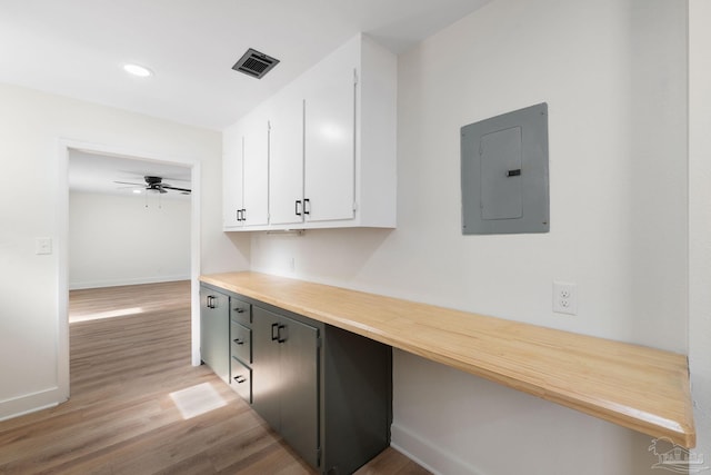 interior space featuring white cabinetry, built in desk, electric panel, ceiling fan, and light hardwood / wood-style floors