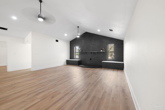 unfurnished living room featuring lofted ceiling, light hardwood / wood-style flooring, ceiling fan, a fireplace, and brick wall